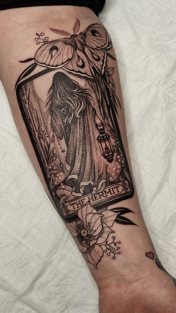 The Hermit tarot card framed by flowers, blackwork tattoo on a forearm
