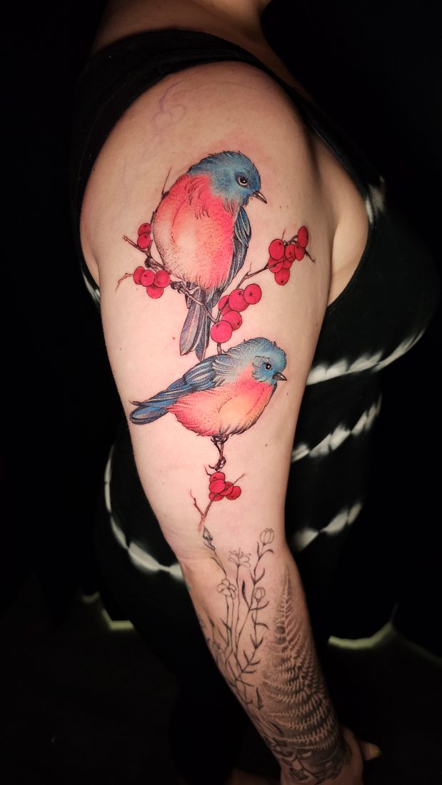 Two bluebirds perched on berries, colour tattoo on an upper arm